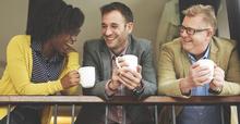 three coworkers holding coffee cups and laughing